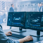 Professional Engineer Works on a Computer with a 3D CAD Software and Tests the Electric Car Chassis Prototype with Wheels, Batteries and Engine Standing in a High Tech Development Laboratory.