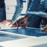 Engineer, Scientists and Developers Gathered Around Illuminated Conference Table in Technology Research Center, Talking, Finding Solution and Analysing Industrial Engine Design. Close-up Hands Shot
